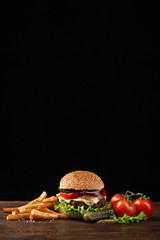 Homemade hamburger close-up with beef, tomato, lettuce, cheese and french fries on wooden table. Fastfood on dark background - obrazy, fototapety, plakaty