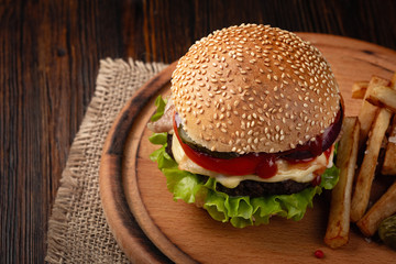 Homemade hamburger close-up with beef, tomato, lettuce, cheese and french fries on cutting board