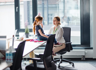 A businesswoman with small daughter sitting in an office, working.