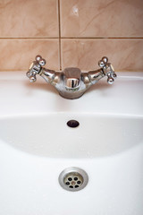 Vertical image of closed  tap over a white bathroom sink