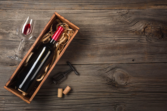 Red wine in a box with a glass and a corkscrew on a wooden table. Top view with space for your greetings