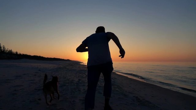 Man running with dog on beach during sunset, super slow motion