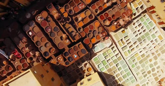 FEZ, MOROCCO. Workers dye skins and hides in the shades of red, blue, brown, green and yellow. Aerial 4K view on tanning industry working process.