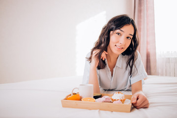 Obraz na płótnie Canvas Tender beautiful caucasian girl in pajamas smiling looking away resting relaxing at home. Amazing joyful brunette woman enjoying morning on bed in hotel room. Relaxation, home comfort.