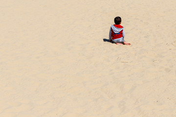 Petit garcon assis sur une plage de sable