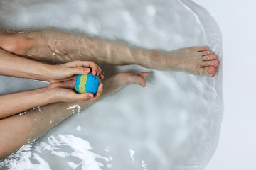 Above shot of woman's legs and hands holding bath bomb in a tub, bodypositive of self care concept