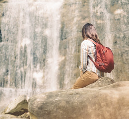 Backpacker woman looking at waterfall on sunny day.