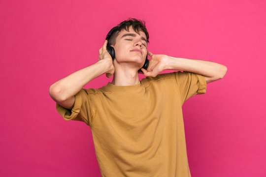 Young Guy Dancing Listening To Music In Headphones On A Pink Background