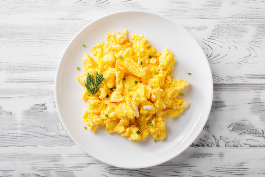 Scrambled eggs on white plate over white wooden background.