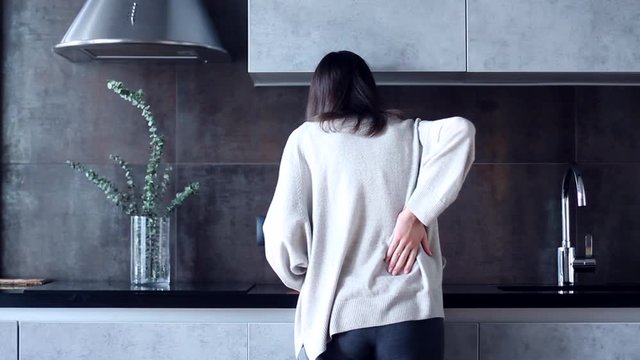 Cute fitness young woman female adult teenager at home in loft kitchen has accodently acute pain in back, suffering and health problem. Health issue, problem with back concept