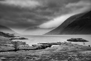 Stunning long exposure landscape image of Wast Water in UK Lake District during moody Spring evening in black and white