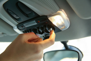 women's hand turns on the light in the car. top panel inside car. 