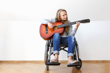 Disabled young woman in wheelchair playing the guitar.