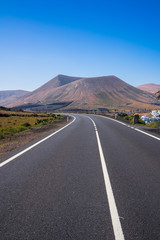 Spain, Lanzarote, Curved black asphalt road through volcanic mountains
