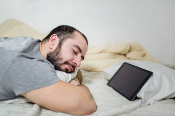 Young and beautiful man sleeps near a tablet.