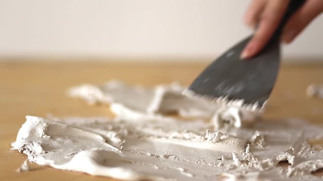 Hand with putty knife, spatula, spackle paste. Girl paints a wooden background, closeup