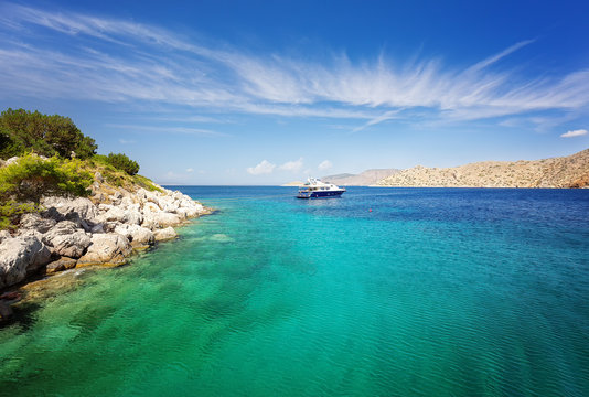 Lagoon in Hydra island, Greece. Crystal clear turquoise water. Luxury yacht with mooring ropes against the rocks.