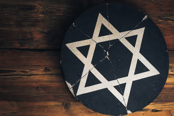 Cracked round stone with a star of David on an old wooden table.
