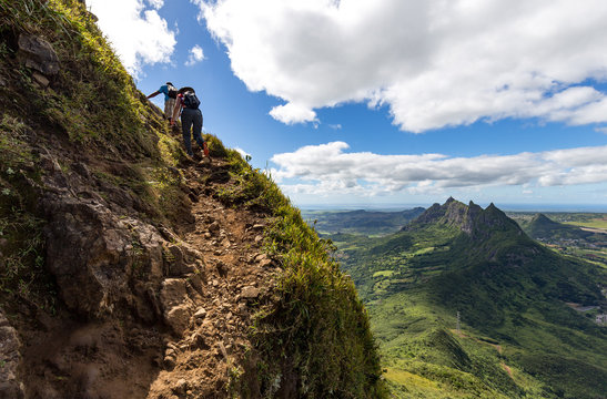 Two persons climbing up the trail to the peak of the mountain Le Pouce on the island of Mauritius with a view over Pieter Both.