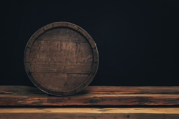 Wooden barrel on a old oak table. Black background behind.