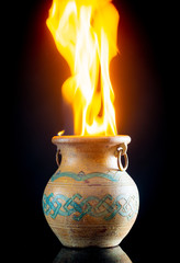 ire burning in ceramic pot with antique ornament on dark background 