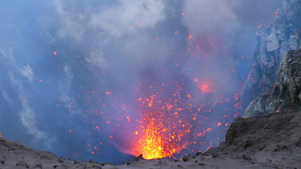 Mount Yasur exploding and belching out mist and hot pieces of glowing magma.