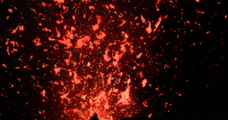 Fototapeta na wymiar CLOSE UP: Active volcanic crater emitting bright pieces of lava during eruption.