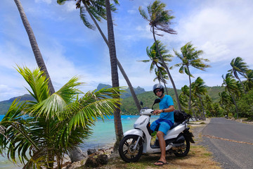 PORTRAIT: Young male traveler sits on a scooter during a road trip in Bora Bora.
