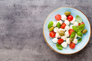Delicious caprese salad with ripe cherry tomatoes and mini mozzarella cheese balls with fresh basil leaves.