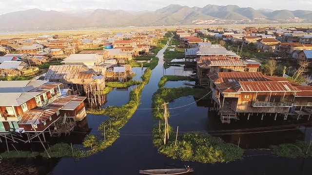 TAUNGGYI, MYANMAR. Aerial drone shot of local vessel passing through the traditional stilt village on Inle Lake. Panorama of the big floating village.
