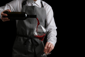 bartender pours wine in glass on dark background