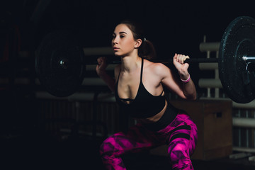 a beautiful sports girl trains a bicep with a rod in her hands in the gym.