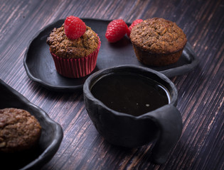 homemade muffin with raspberry and black clay dish on a rustik style wood table