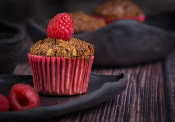 homemade muffin with raspberry and black clay dish on a rustik style wood table