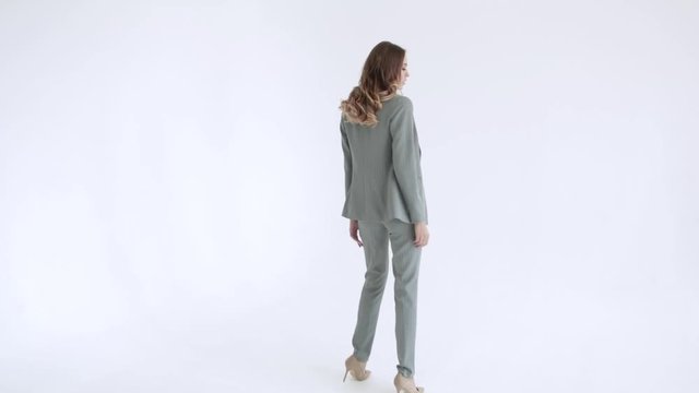 Business lady posing in a gray jacket and trousers on a white background. Sexy female model, in gray suit goes ahead, 50 frames per second
