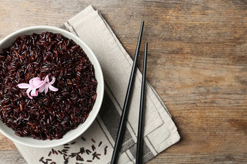 Flat lay composition with bowl of boiled brown rice and space for text on wooden background