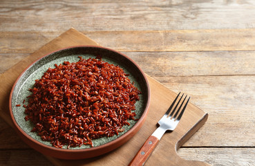 Board with plate of boiled brown rice and fork on table. Space for text
