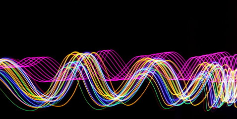 Pink and multi color light painting photography, long exposure, gold, pink, green and blue waves of vibrant color against a black background