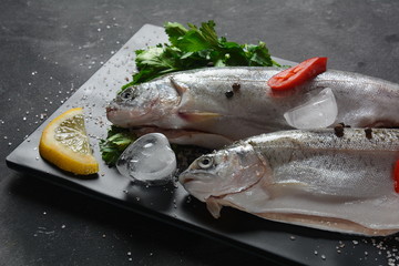 Fresh trout with salt, pepper, lemon on dark background 