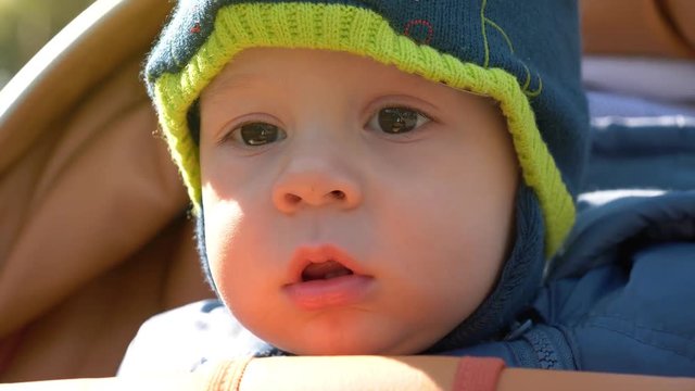 Little baby boy with open mouth sits in perambulator close up