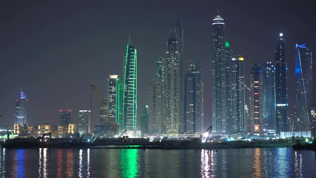 Construction equipment, excavator works at night. Nightly Dubai preparing to Expo 2020, building construction. View from sea or Palm to JBR quay with modern skyscrapers. UAE