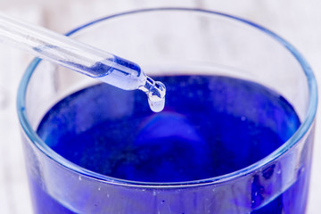 Pipette drops a drop of liquid into a blue liquid container