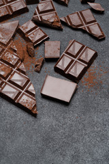 Dark or milk organic chocolate pieces and cocoa powder on dark concrete backgound