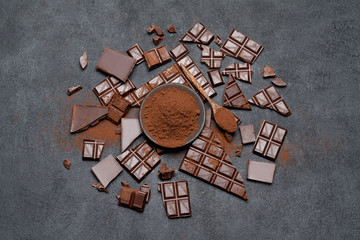 Dark or milk organic chocolate pieces and cocoa powder on dark concrete backgound