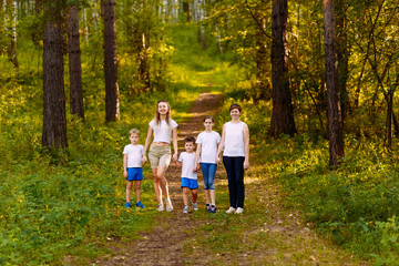 Fototapeta premium two women and three children walk through the forest, holding hands. in full growth summer