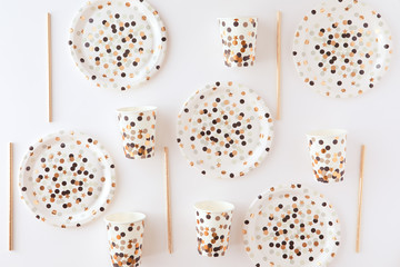 Golden and black paper glasses, dishes and straws on a white table. Party flat lay and top view...