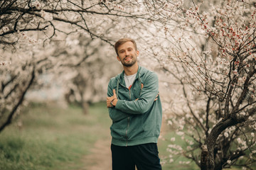 A young happy man stands among the blossoming garden.