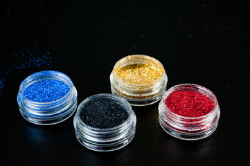 Colorful paillettes for nails in plastic jars on a black background