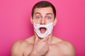 Impressed surprised emotional man puts his hand on chin, opens his mouth and blue eyes widely,...
