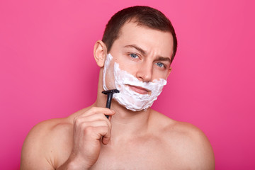 Close up portrait of thoughtful handsome brunette model posing in front of camera, shaves, makes his skin smooth, looks attentive. People, beauty and care concept. Copy space for advertisement.
